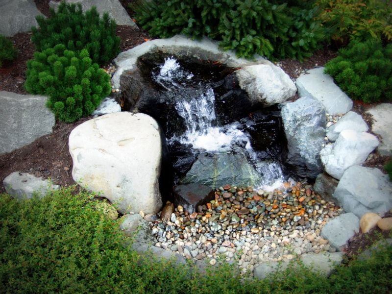 a small waterfall is surrounded by rocks and plants in a garden