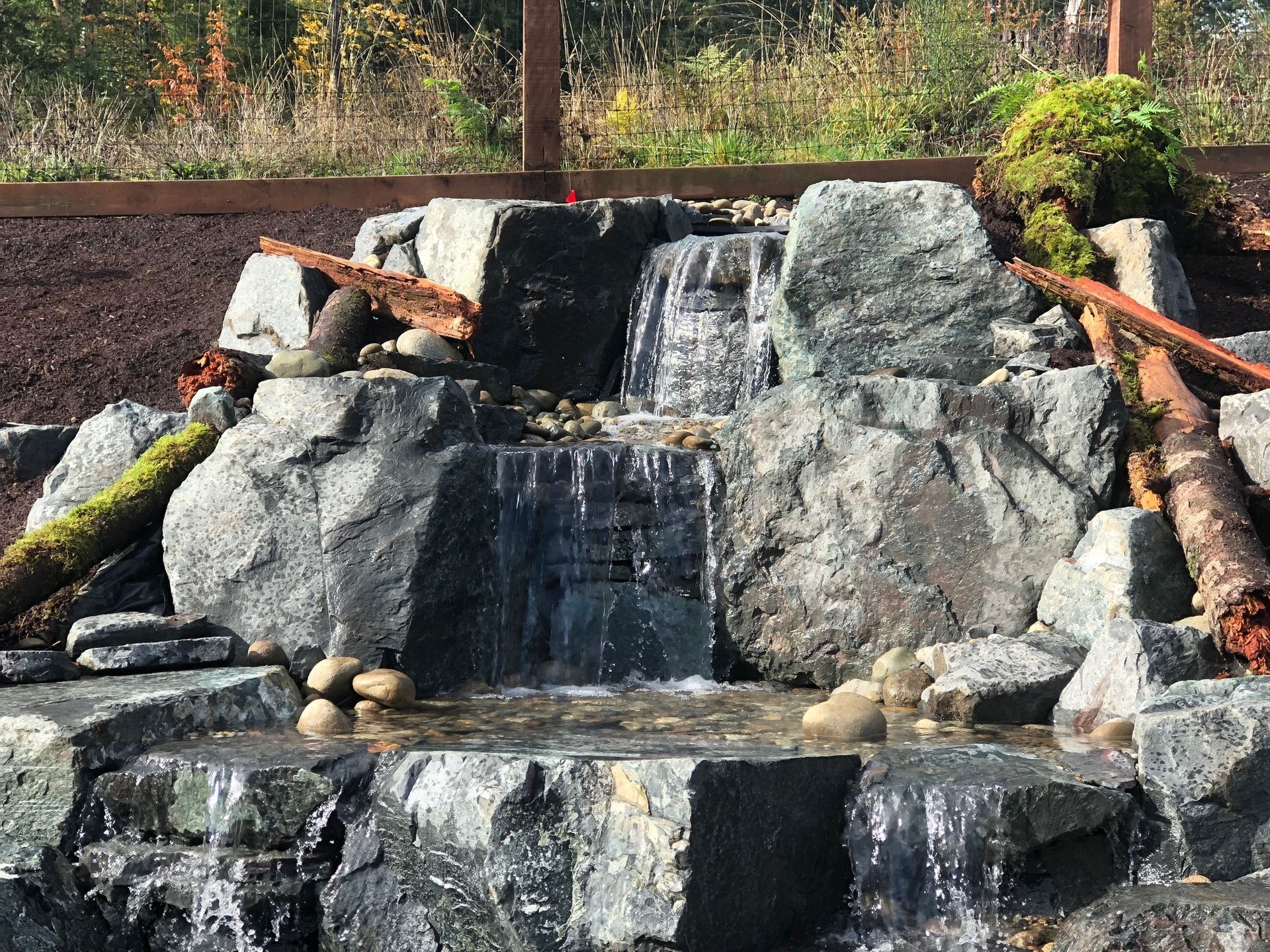 a waterfall is surrounded by rocks and trees in a garden