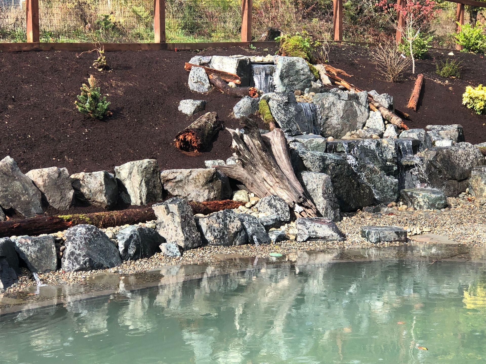 a pond surrounded by rocks and a fence with a waterfalls