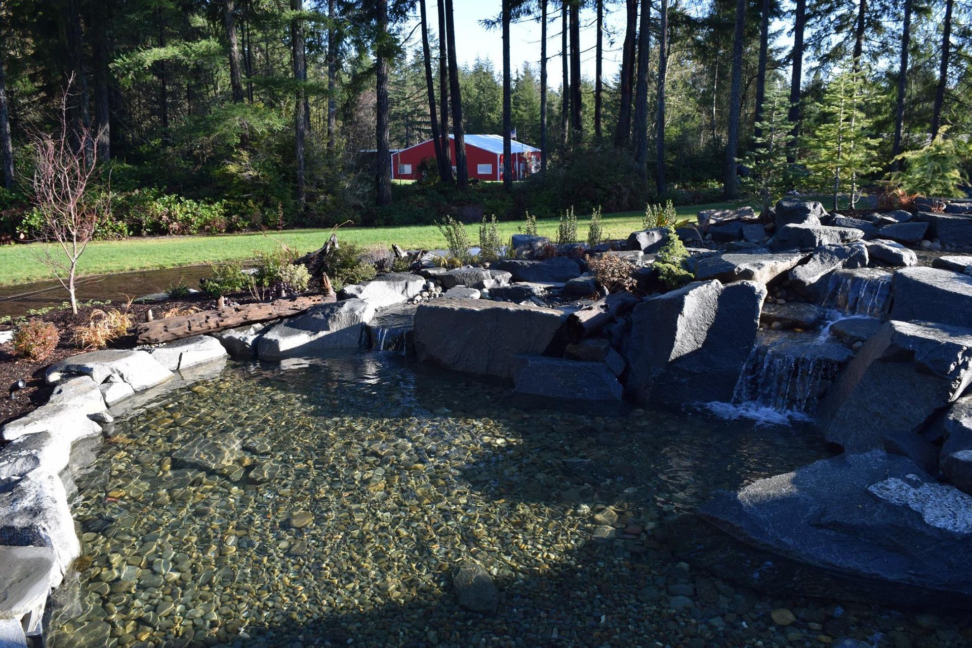 a pond surrounded by rocks and trees with a red barn