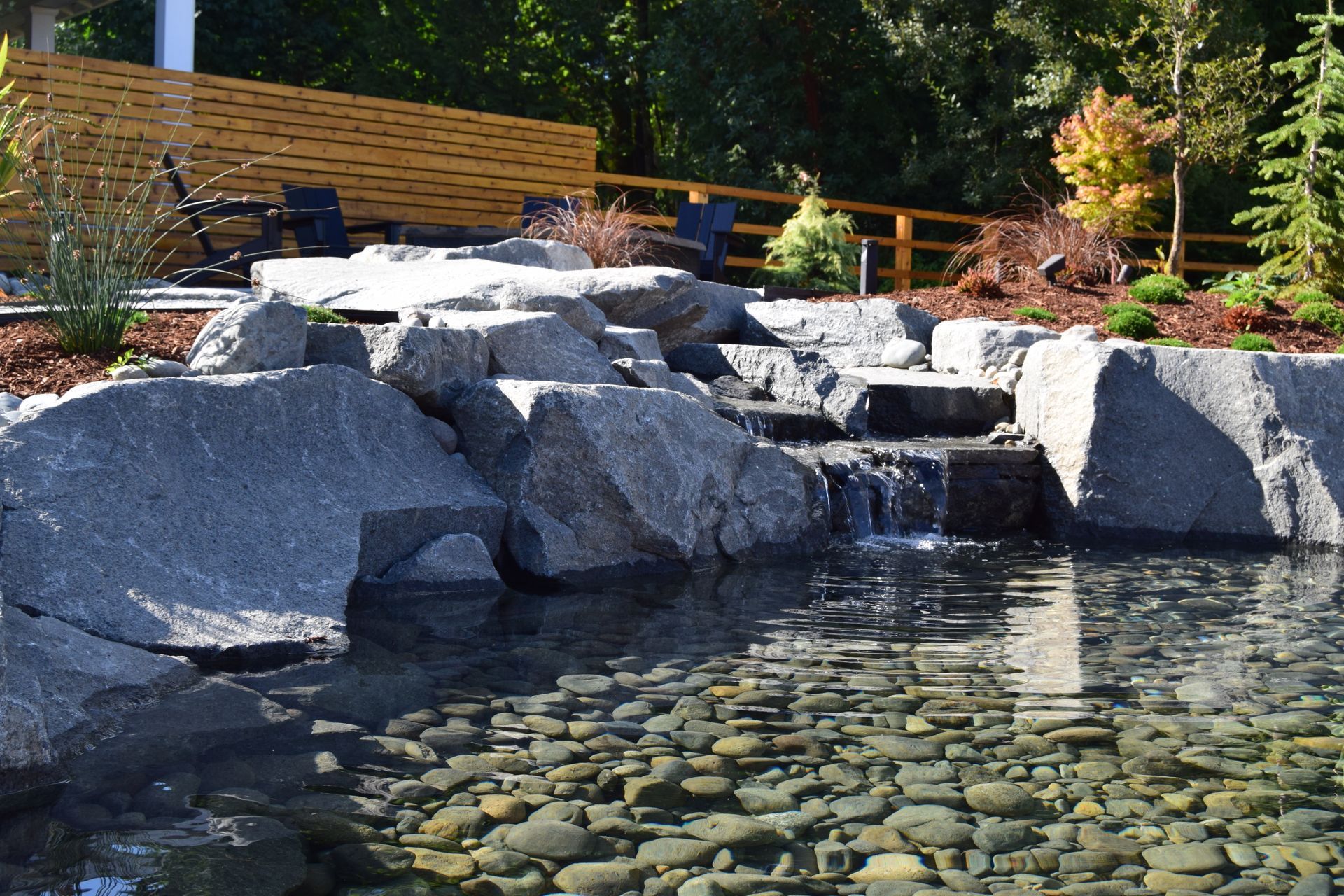 a pond surrounded by rocks and trees with a wooden fence