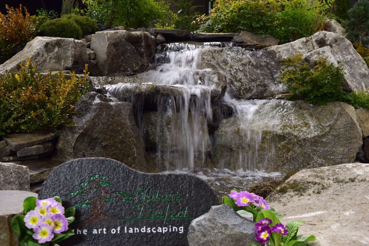 a waterfall is surrounded by rocks and flowers in a garden