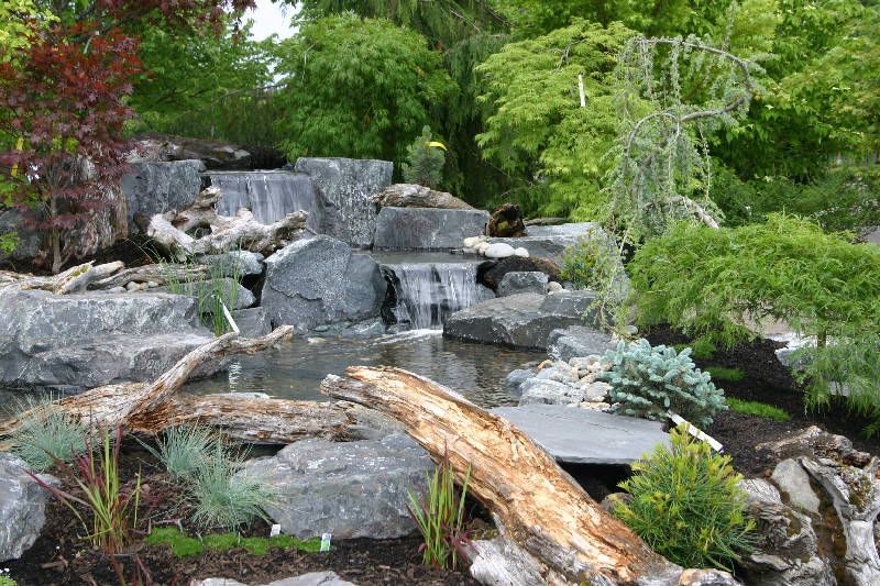 a waterfall is surrounded by rocks and trees in a garden