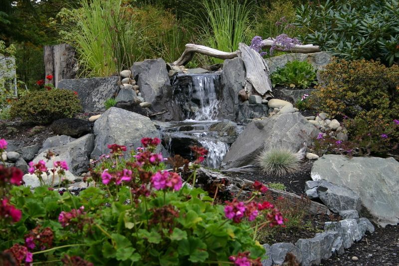 a waterfall is surrounded by rocks and flowers in a garden