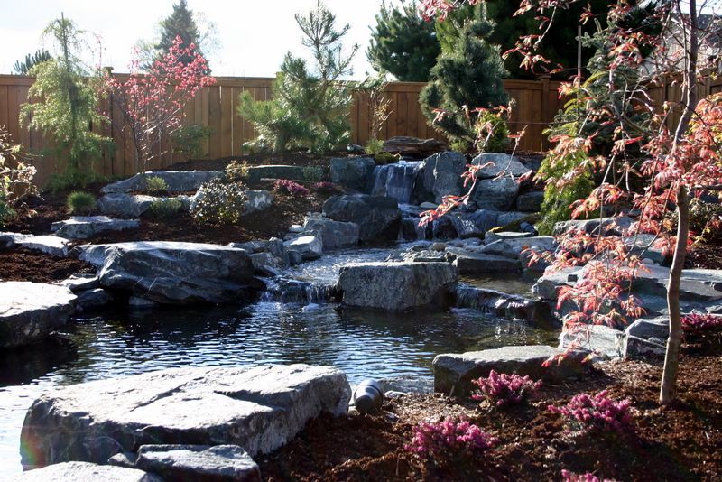 a pond surrounded by rocks and trees with a wooden fence in the background