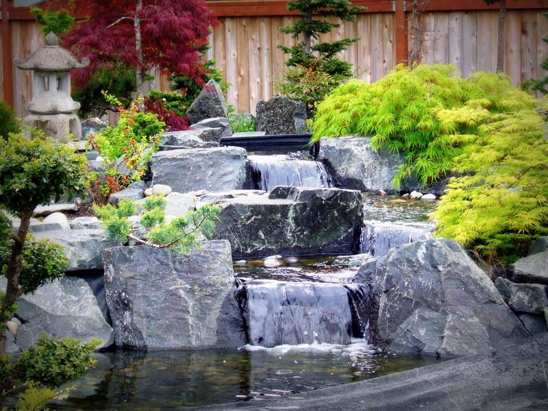 a waterfall is surrounded by rocks and trees in a garden .