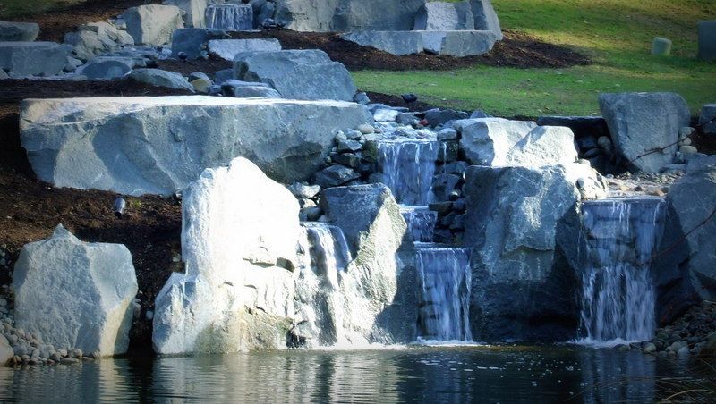 a waterfall is surrounded by large rocks and a pond