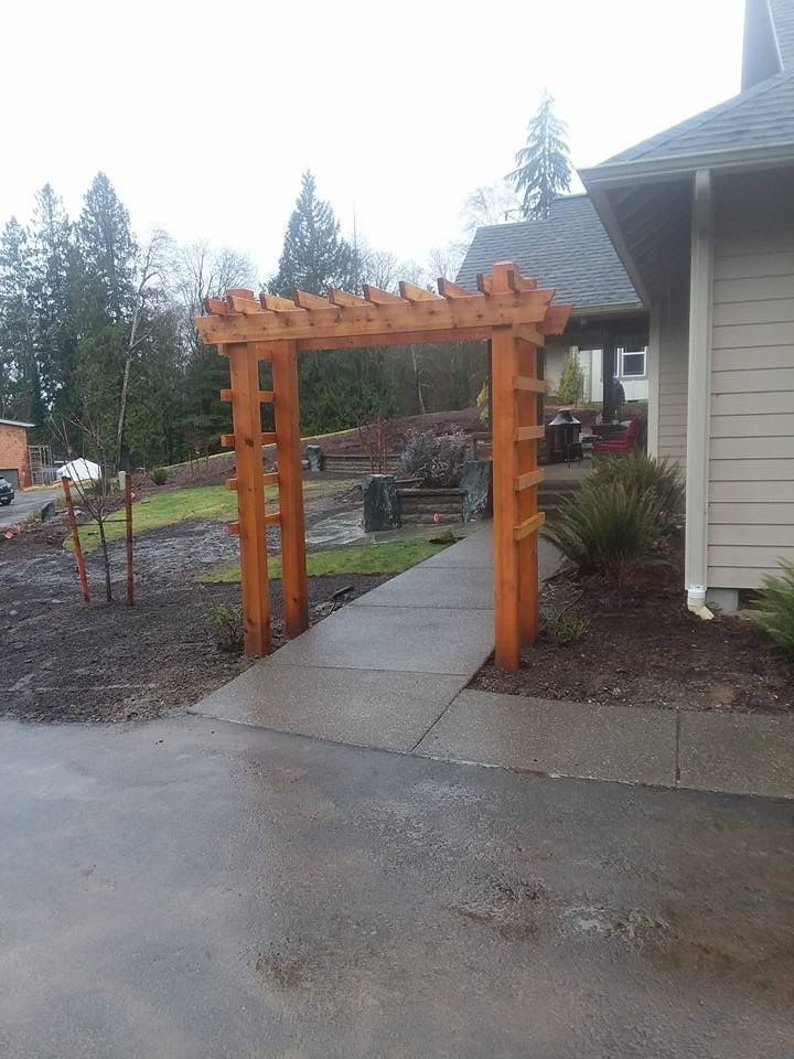 a wooden archway leading to a house with trees