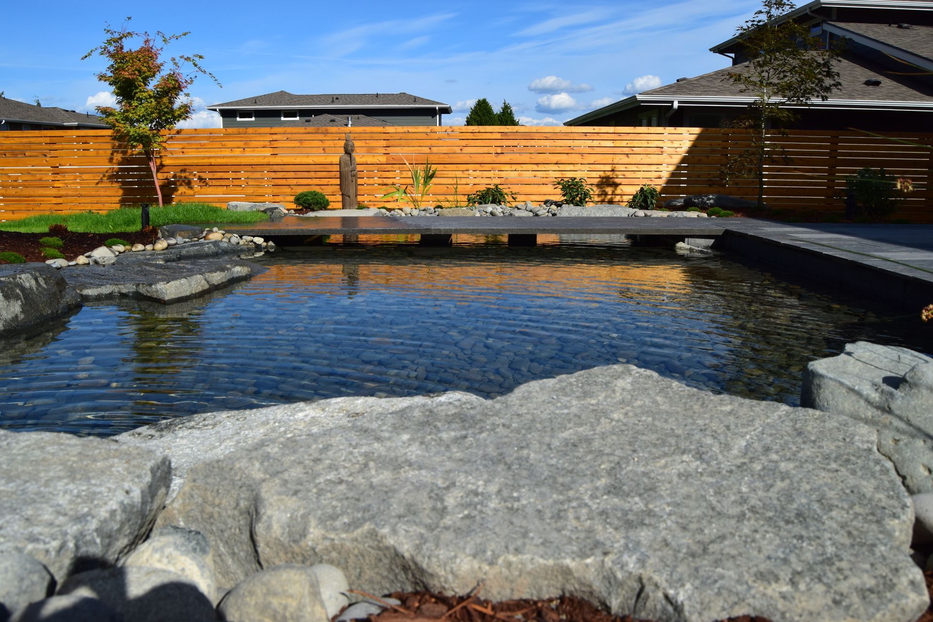 a large pond surrounded by rocks and a wooden fence in a backyard