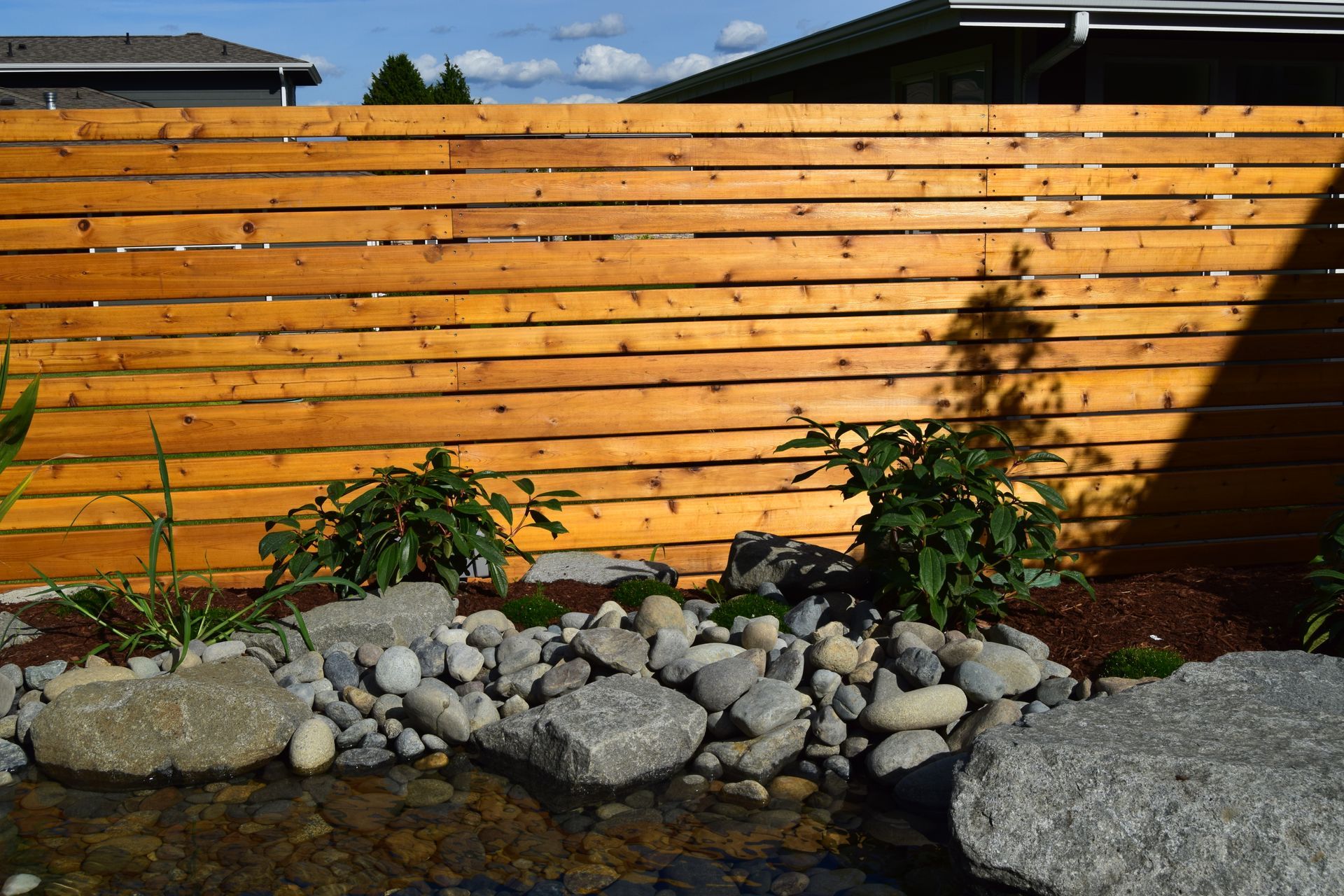 a wooden fence surrounds a pond with rocks and plants