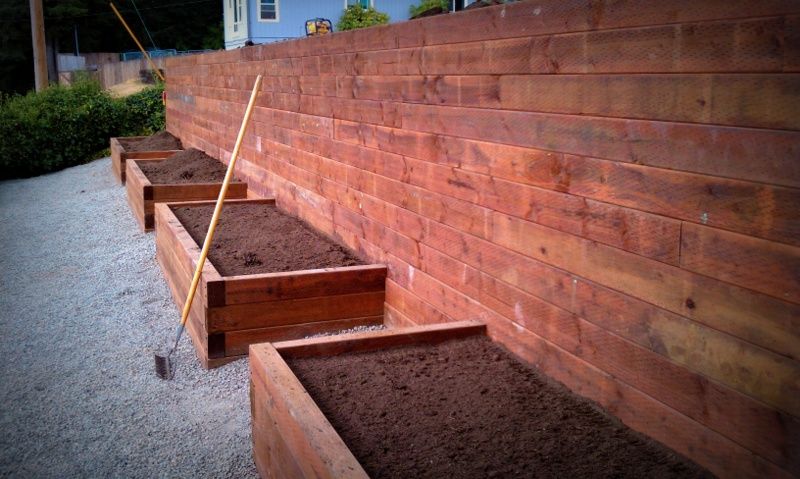 a row of wooden planters filled with dirt next to a wooden fence