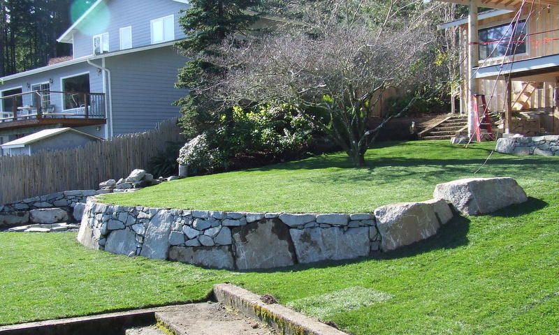 A stone wall surrounds a lush green lawn in front of a house.