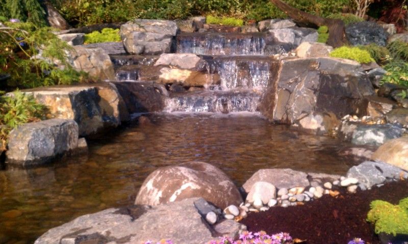 A waterfall is surrounded by rocks and flowers in a garden.