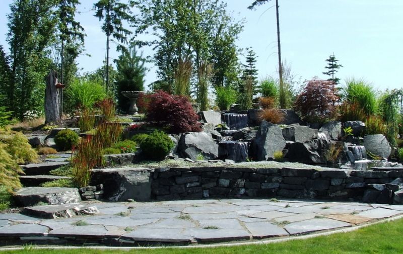 A garden with a stone wall and a waterfall in the background