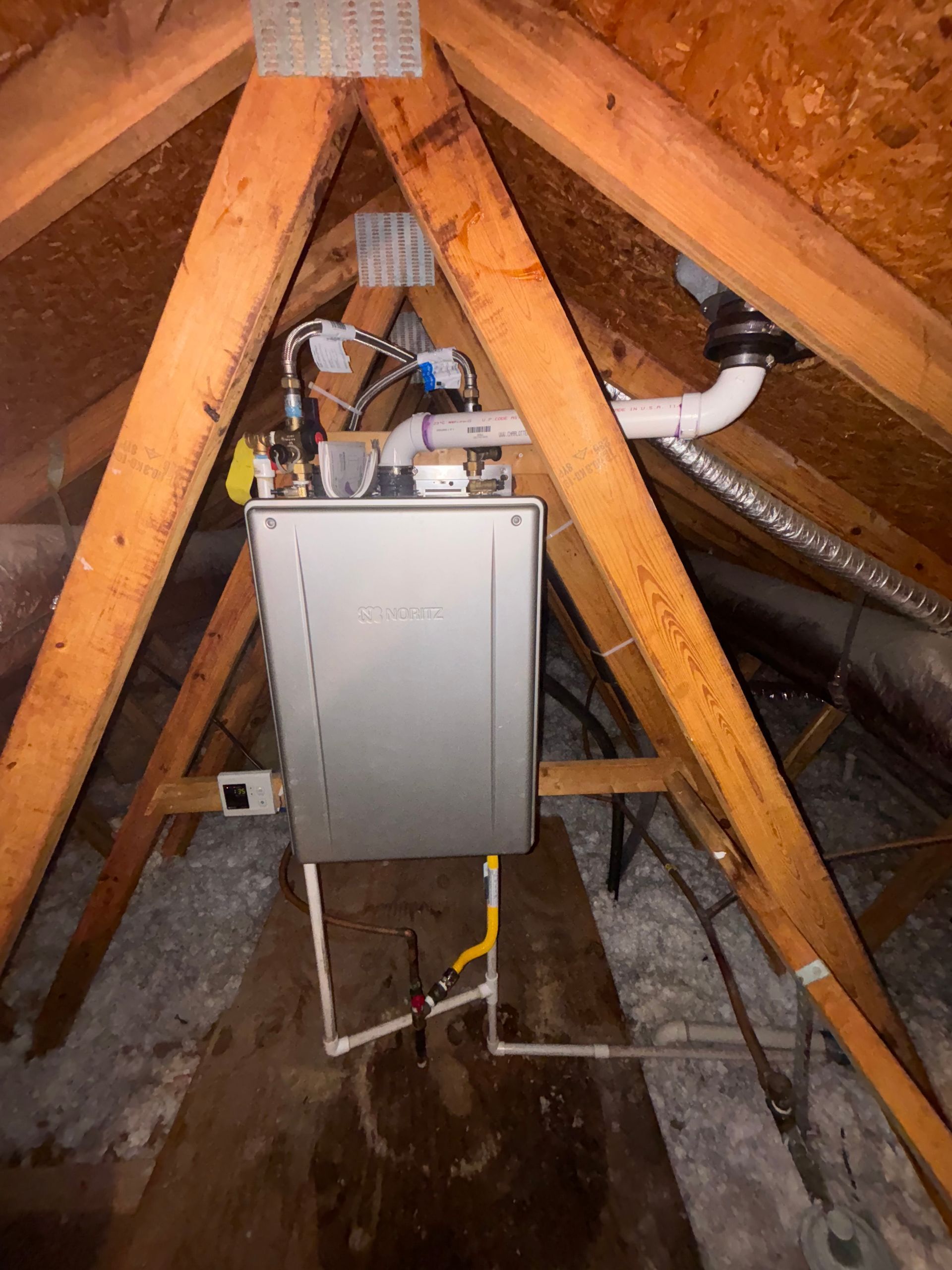 A gas water heater installed in an attic. Wooden beams, white pipes, and vent pipe visible.