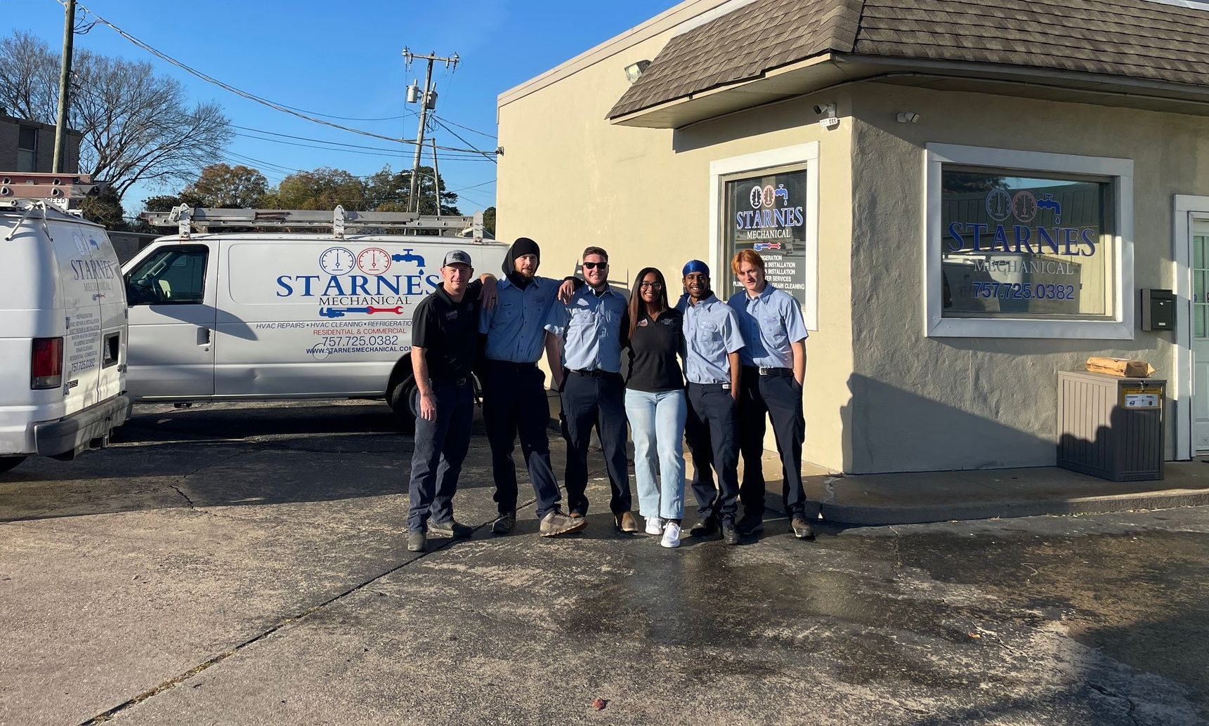 Group of people standing in front of a building with a company van, under a sunny sky.