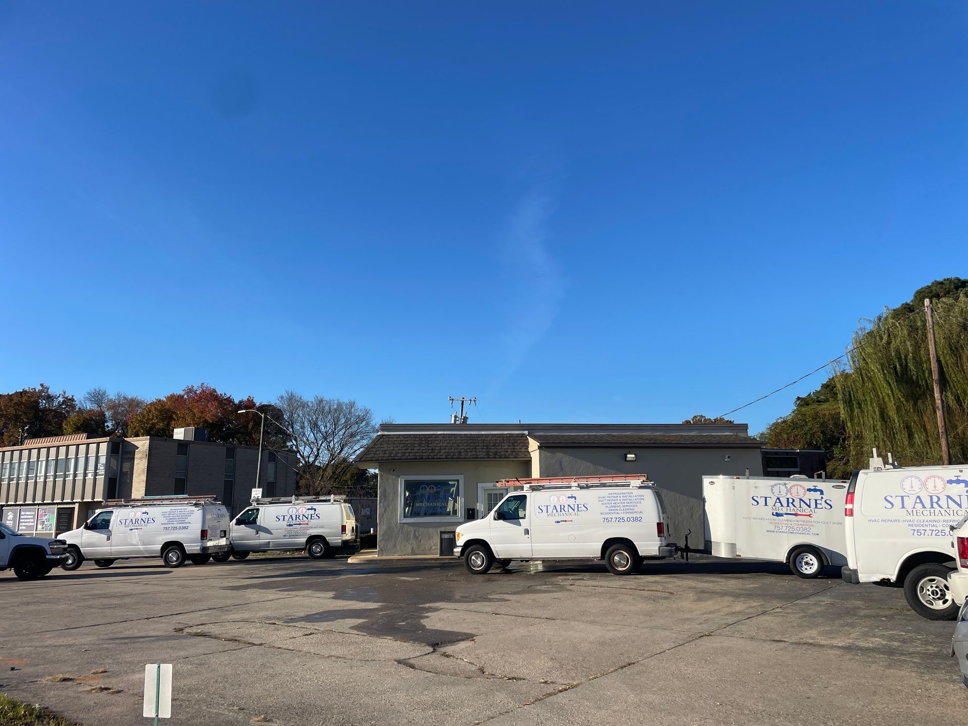 Several white service vans parked in front of a building with blue sky background.