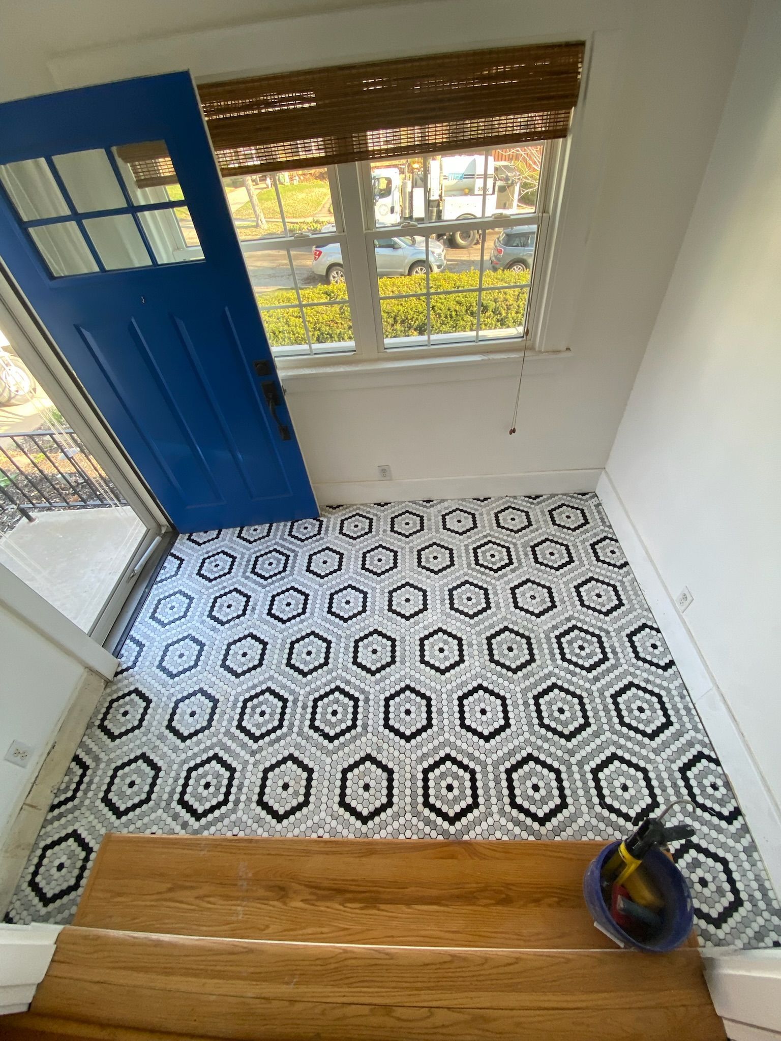 Looking down at entry: blue door, patterned floor tiles, window with sunlight, brown wooden stairs.