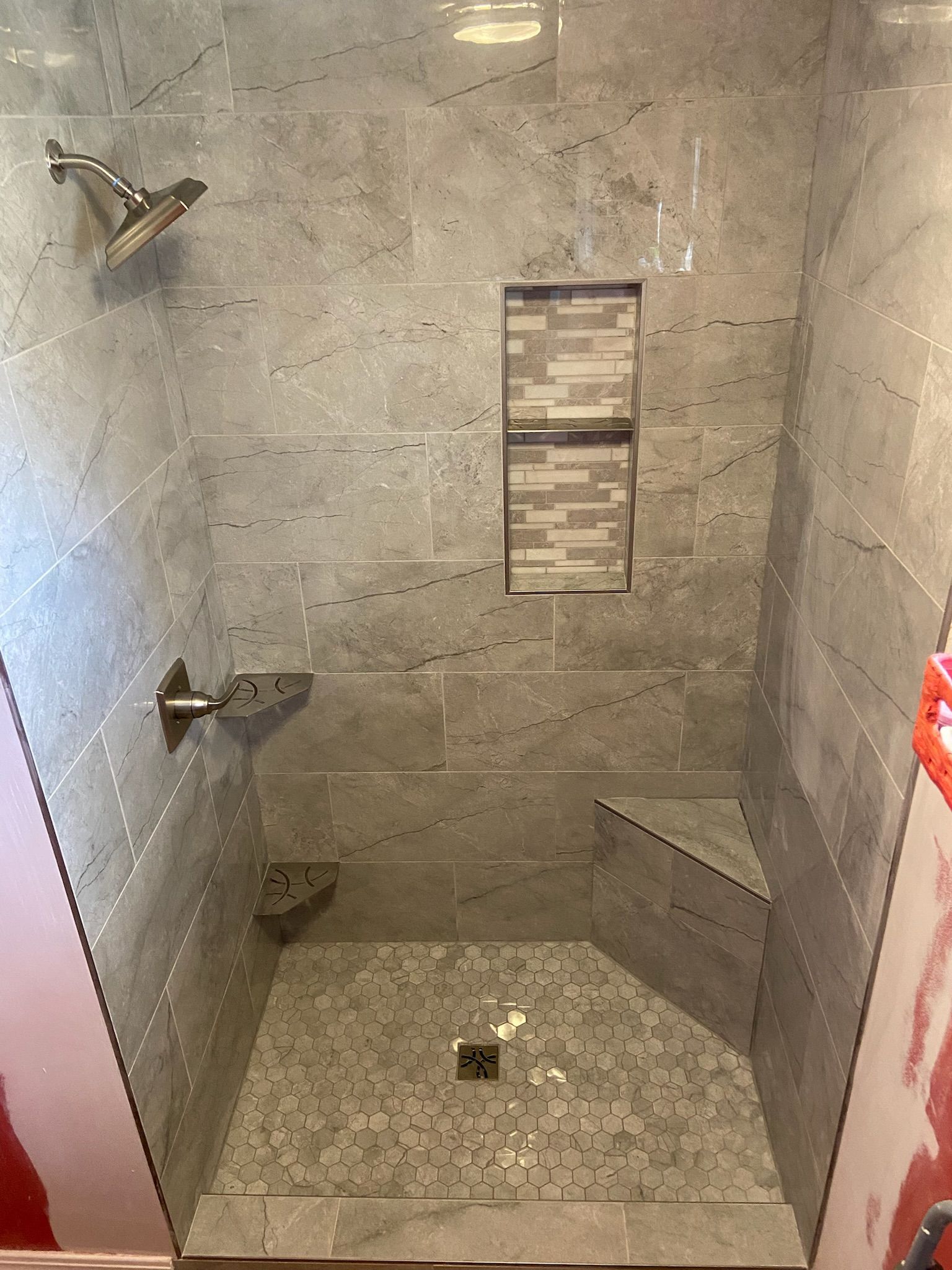 Gray tiled shower with built-in bench, shelf, and niche. Silver showerhead and fixtures.
