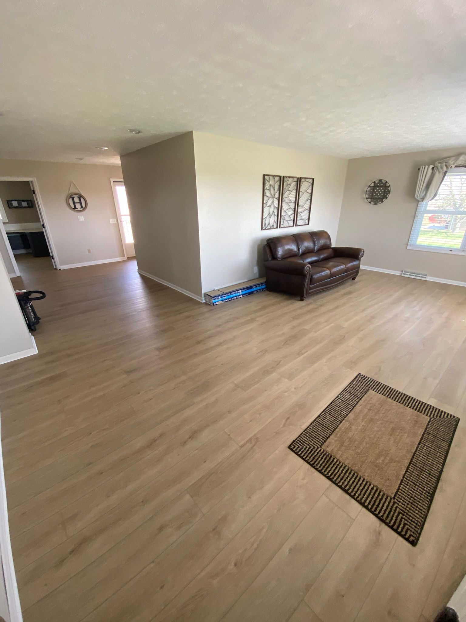 Spacious living room with light wood floors, brown couch, and rug. Gray walls and doorway leading to other rooms.