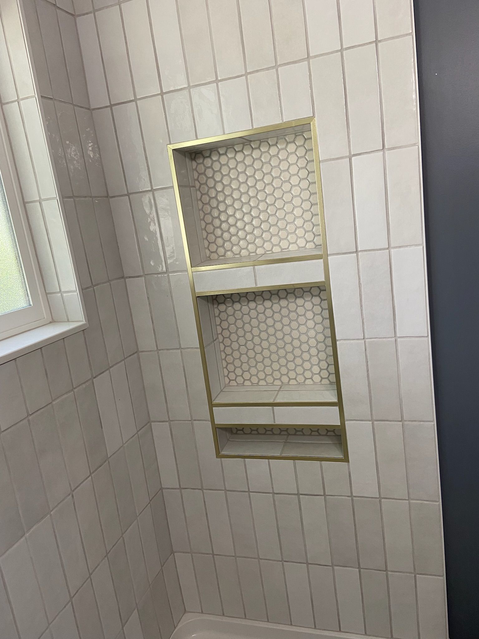 Tiled shower niche with honeycomb tile backing and shelves, in a bathroom.
