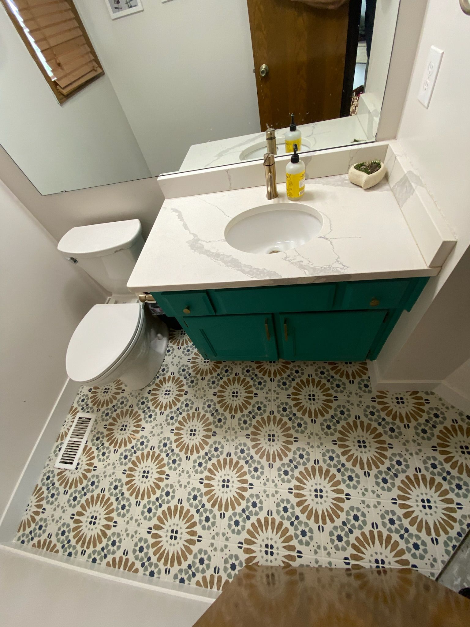 Bathroom with teal vanity, patterned tile floor, toilet, and mirror.