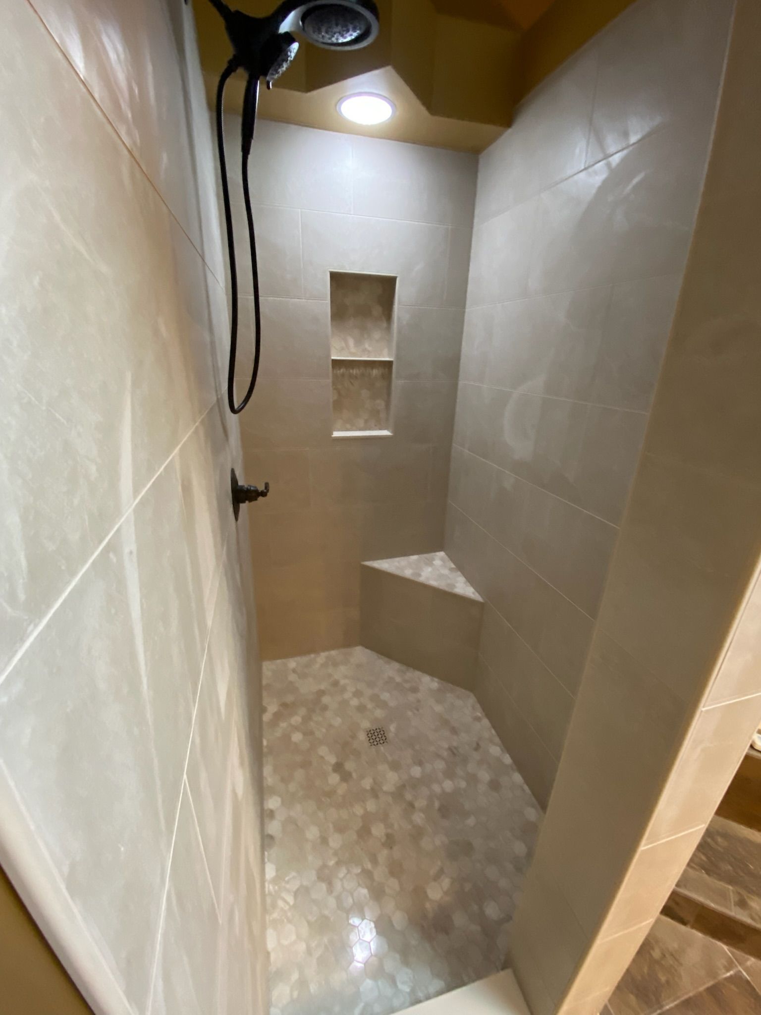 Neutral-toned tiled shower with built-in bench and recessed shelves; black shower fixtures.