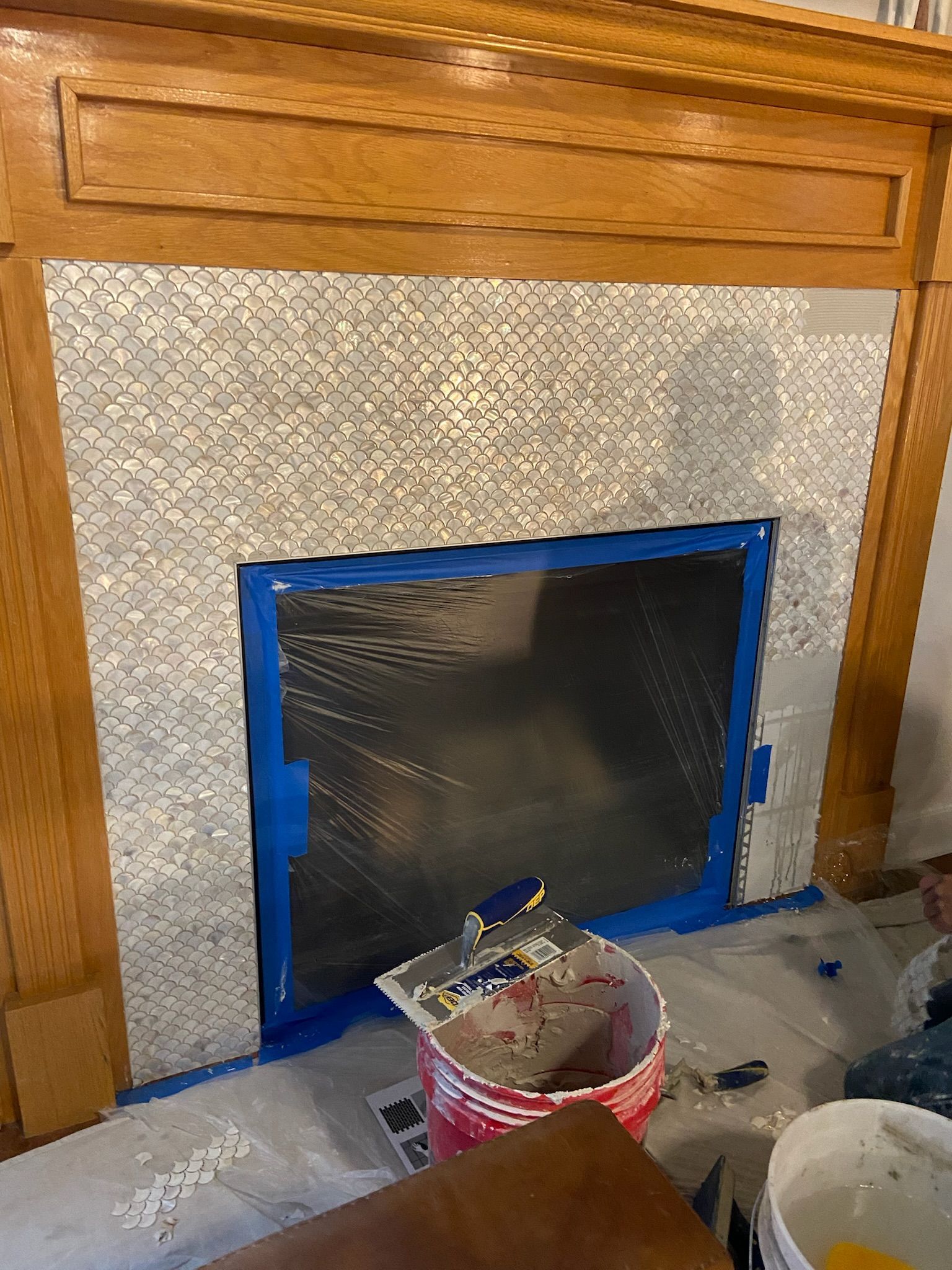 Fireplace with new patterned tile installation; blue tape frames the opening.