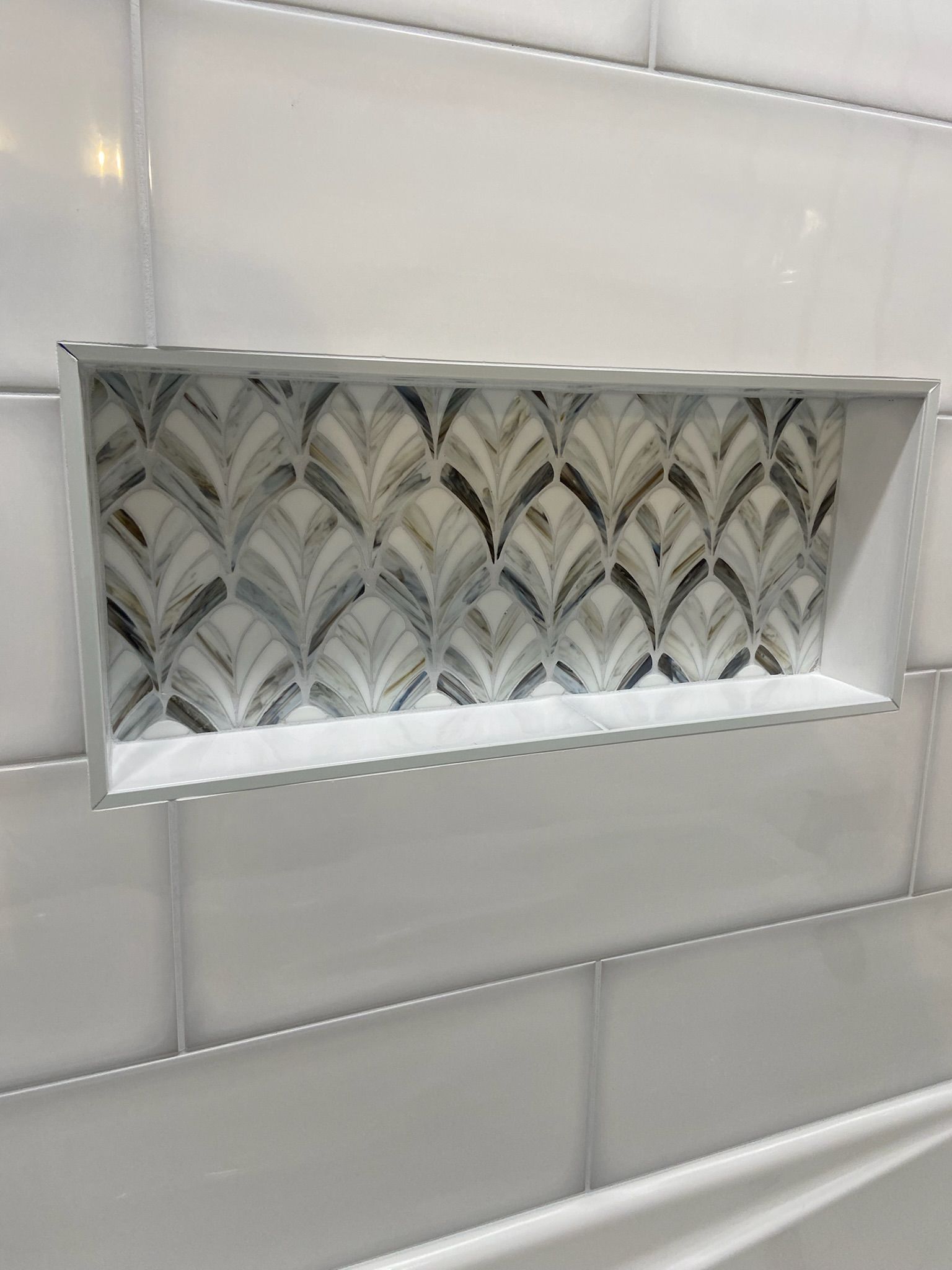 White tiled shower wall with a decorative mosaic tile niche.