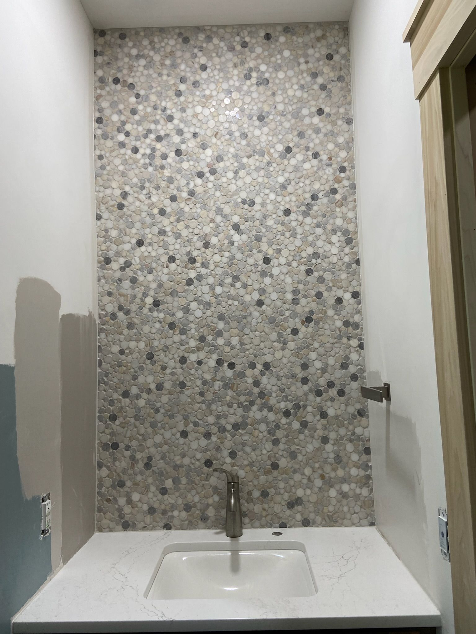 Small bathroom with mosaic tile accent wall, white countertop, and silver faucet.