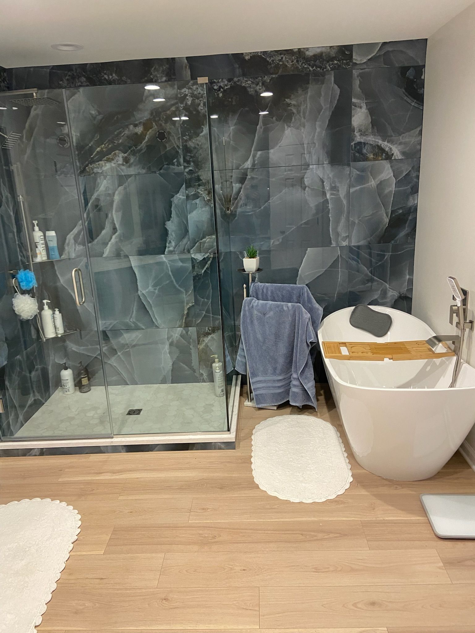 Modern bathroom with large blue tile shower, freestanding tub, and wood-look flooring.