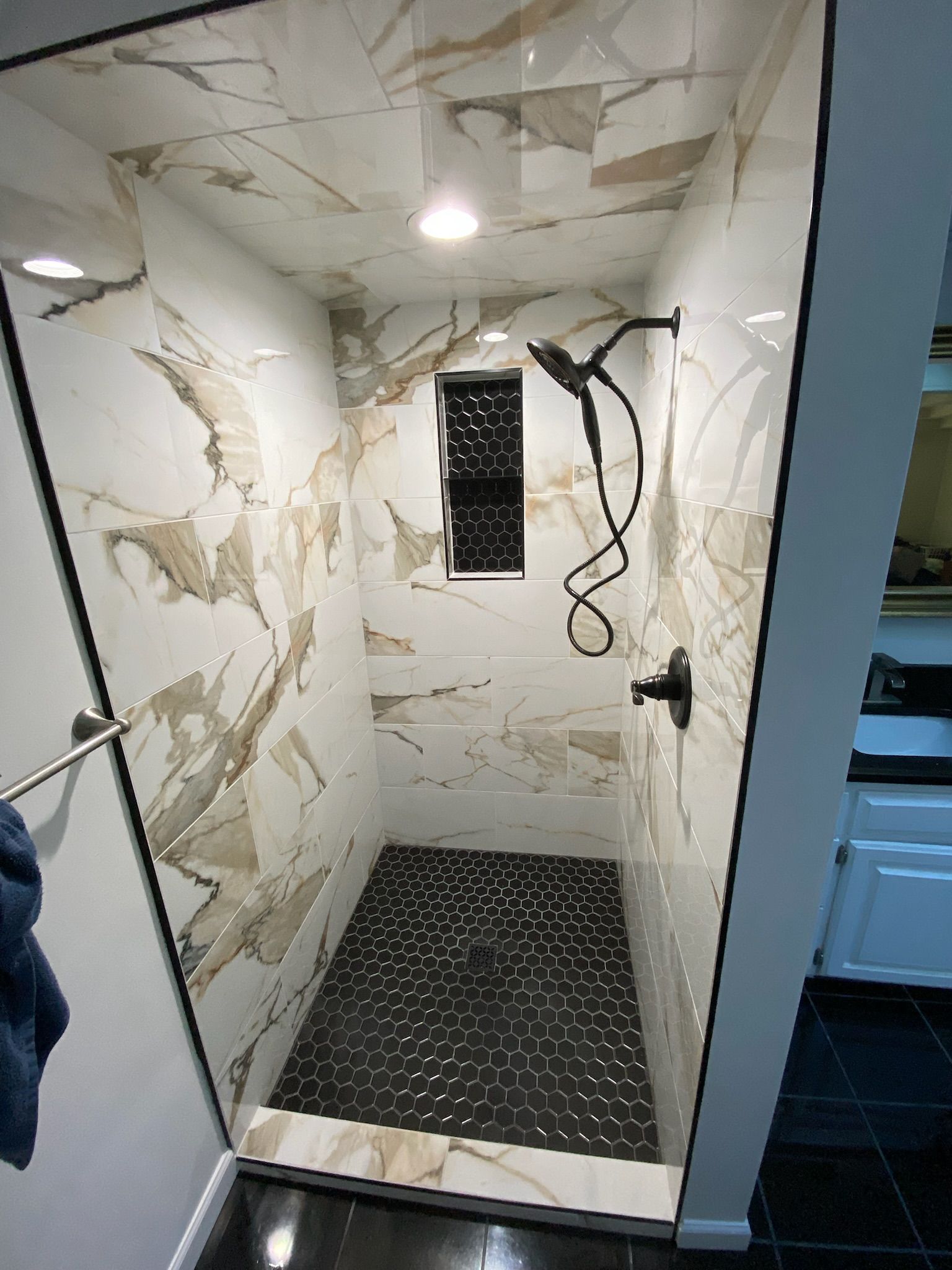 Modern shower with marble and pebble tile, black fixtures, and recessed lighting.