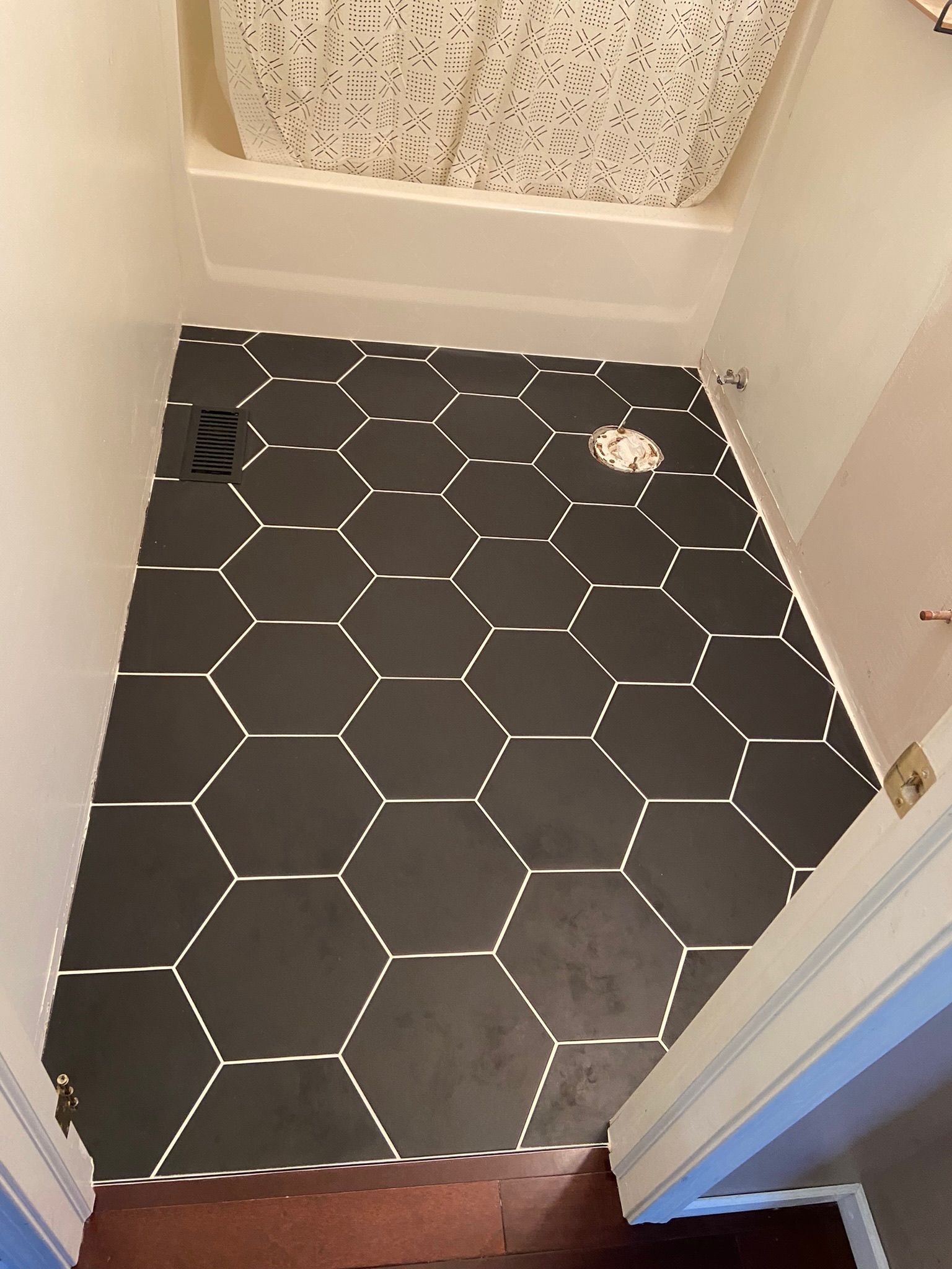 Bathroom floor with black hexagon tiles, white grout, and a shower with a patterned curtain.