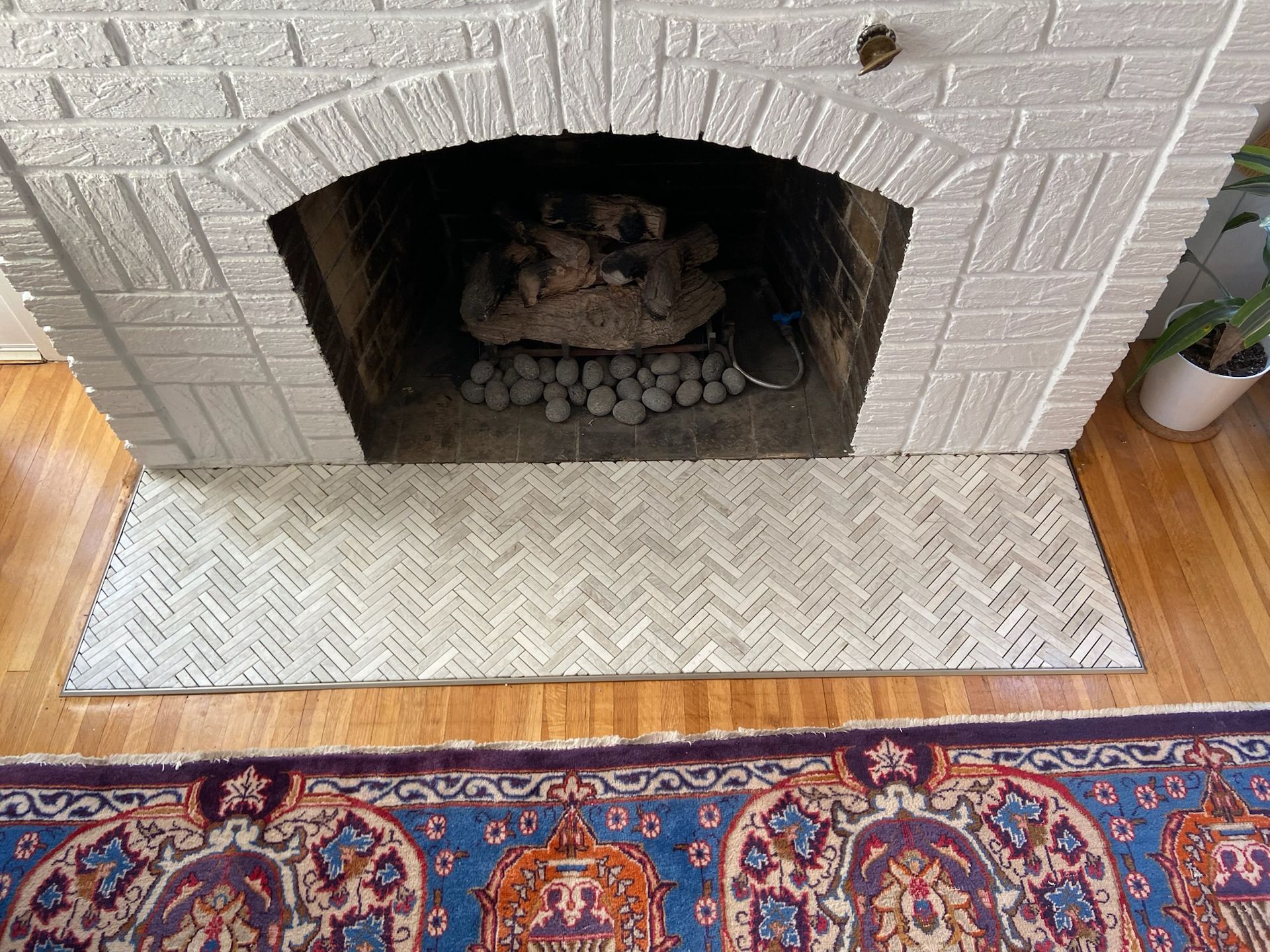 White brick fireplace with logs inside, sitting on a patterned rug.