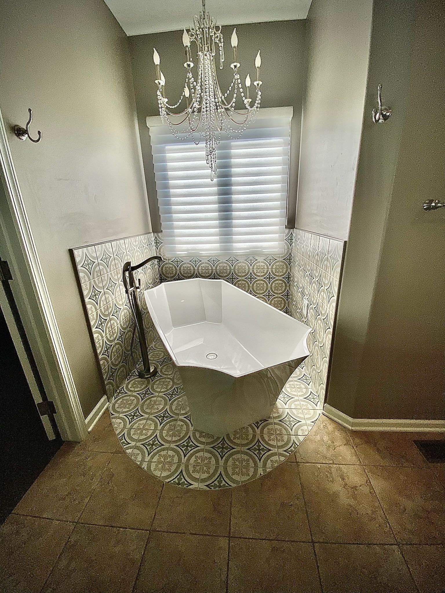 Bathroom with a white freestanding bathtub, mosaic tile surround, and a chandelier.