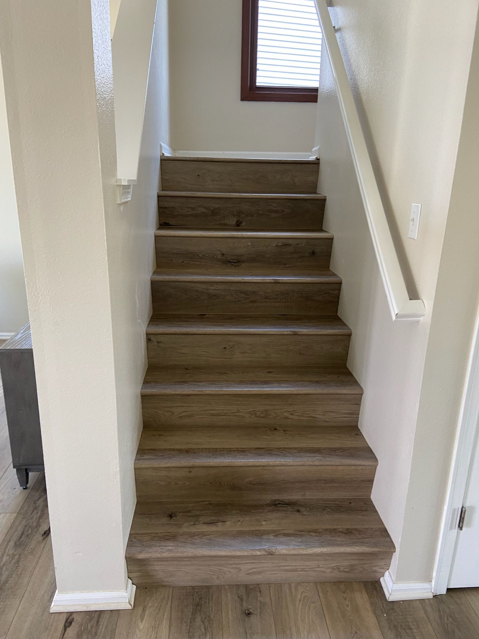 Wooden staircase with cream-colored walls and a window at the top.
