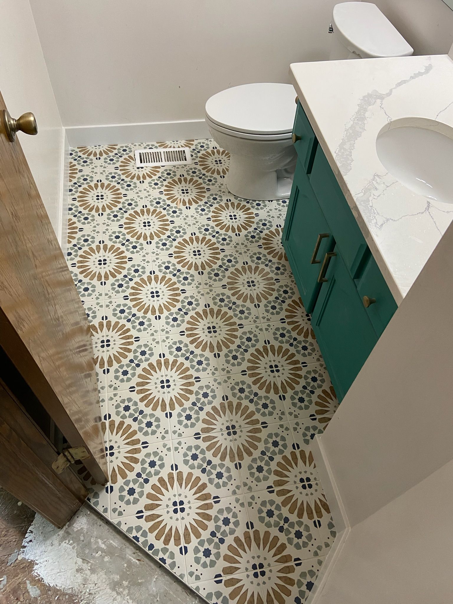 Bathroom with patterned floor tiles, teal vanity, and white toilet.