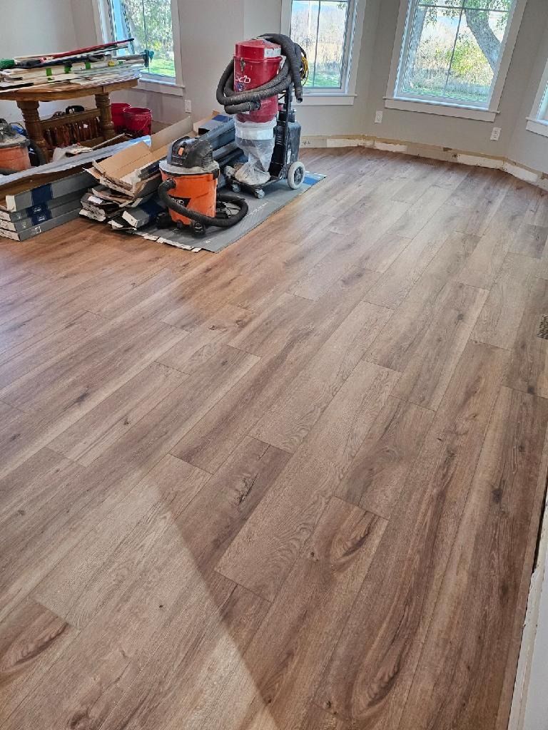 Newly installed wood-look flooring in a room with a large window and equipment for floor refinishing.