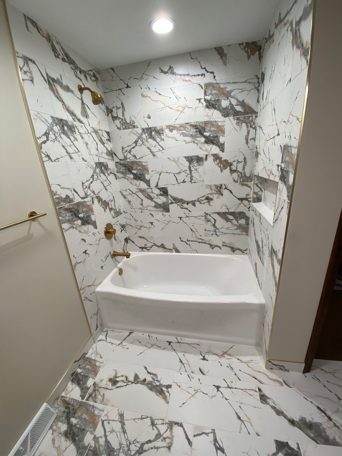 Small marble-tiled shower with a built-in bench and brass grab bars in a narrow bathroom.
