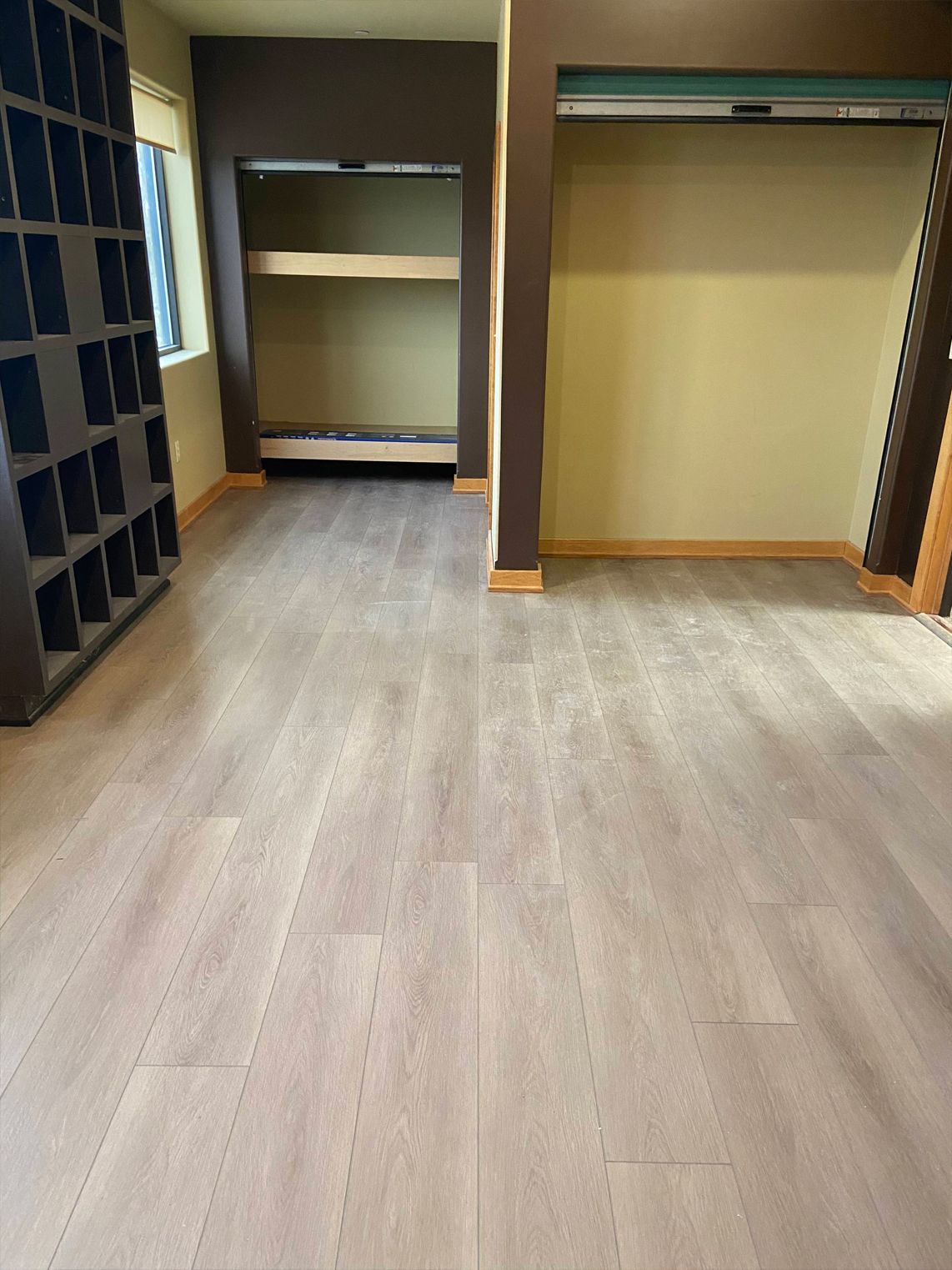 Empty closet with shelves and hanging rods, light wood floor, and tan walls