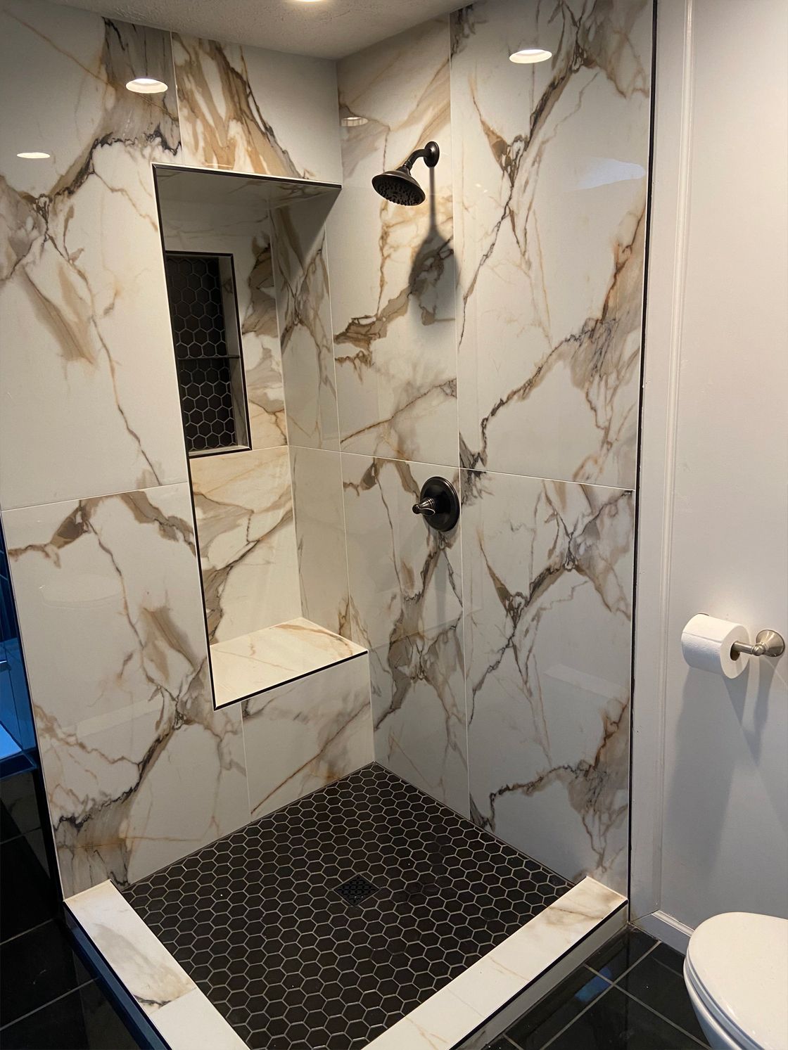 Modern shower with marble-look tile walls, black shower floor, and built-in mirror niche.
