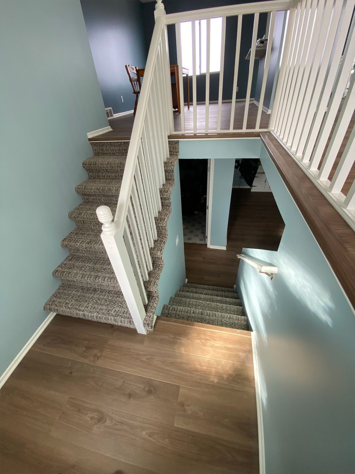 Staircase with white railing, wood floor, and carpeted steps in a light blue hallway.