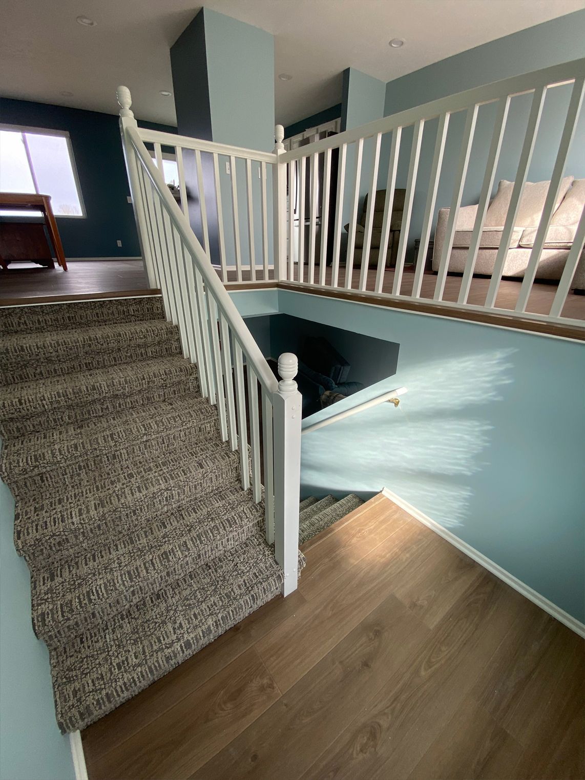 Staircase with white railing beside a carpeted landing and wood floor in a bright home interior