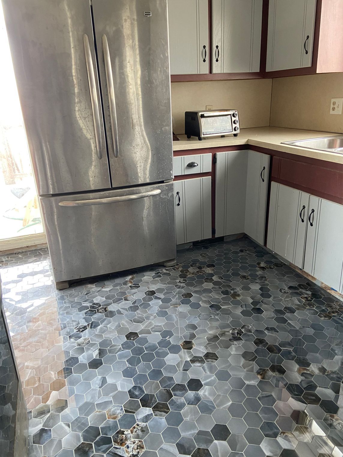 Small kitchen with stainless steel fridge, white cabinets, brown counters, and hexagon tile floor.