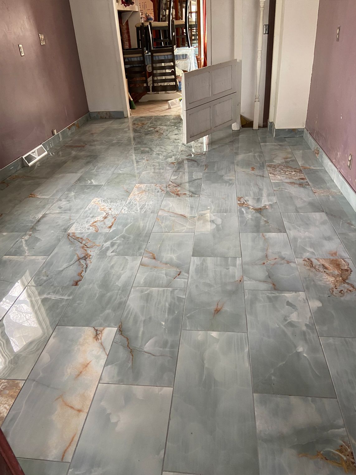 Narrow indoor hallway with gray marble tile flooring and pink walls, partially under construction.