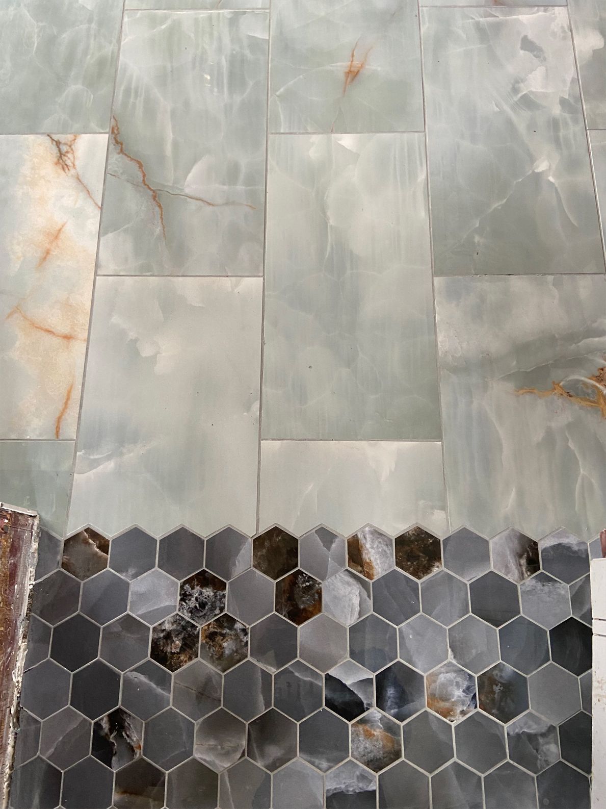 Gray marble wall tiles above a dark hexagonal mosaic floor with some cracked and missing pieces