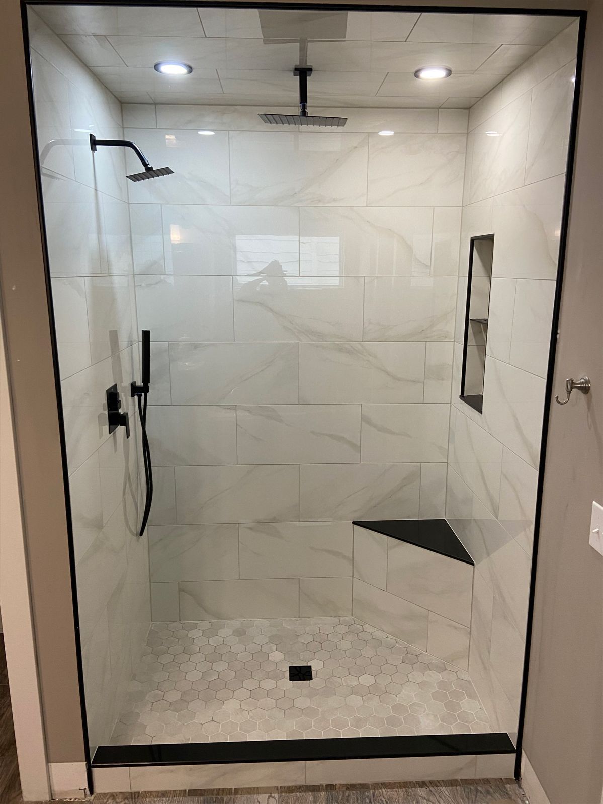 Empty modern tiled walk-in shower with rainfall showerhead and glass door.