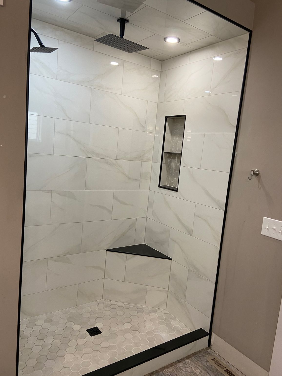 Modern tiled walk-in shower with glass entry, built-in niche, and a corner bench.