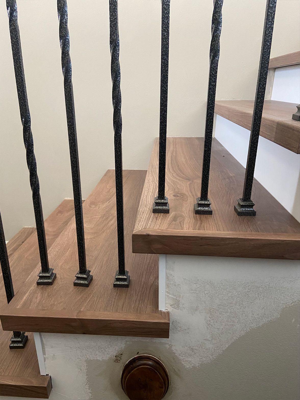 Staircase with wooden steps and black metal railings along a beige wall