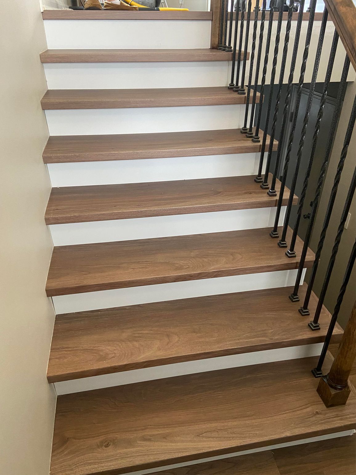 Wooden staircase with white risers and black metal railing, viewed from below.